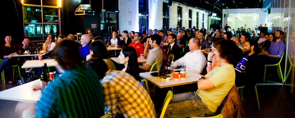 People, audience watching Simon Pampena, ABC broadcaster, at microphone. Ultimo Science Festival event: Stand up science comedy night in Santos cafe, level 3.